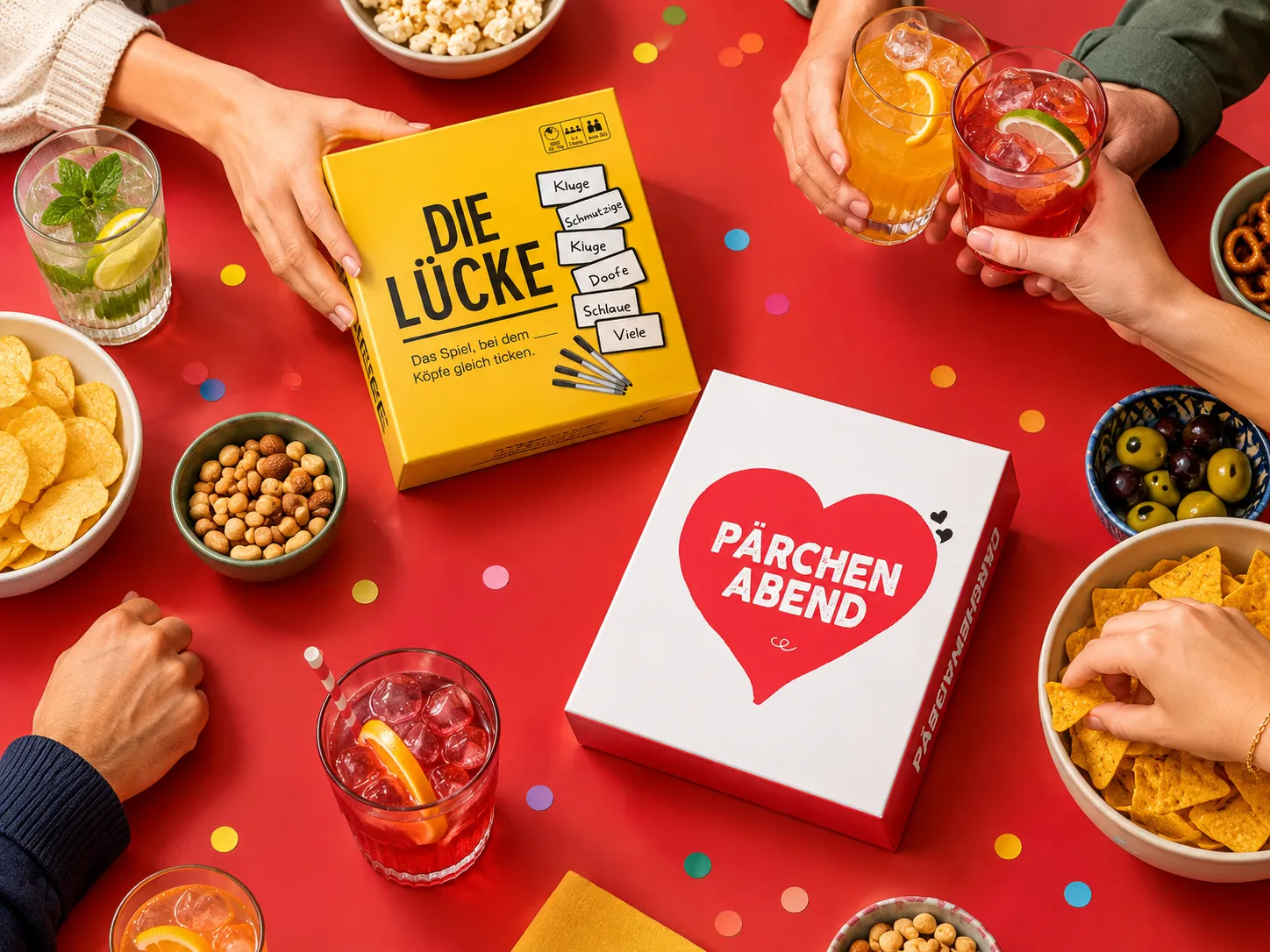 Freunde greifen am Tisch nach den Spielen Die Lücke und Pärchenabend, daneben Getränke und Snacks